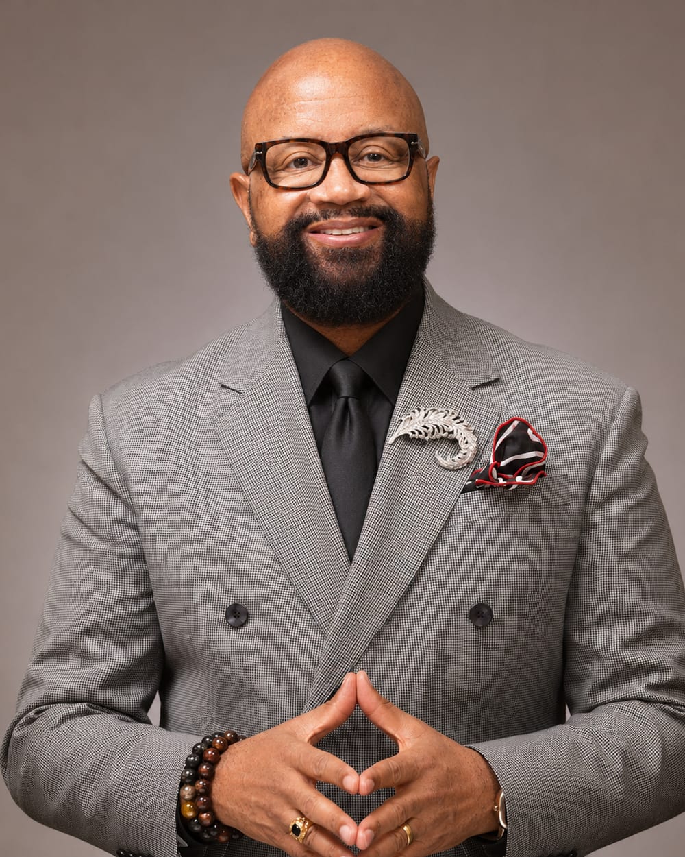 Portrait of Bishop Donald Hilliard, Jr. in a grey houndstooth suit, hands clasped, looking toward the viewer